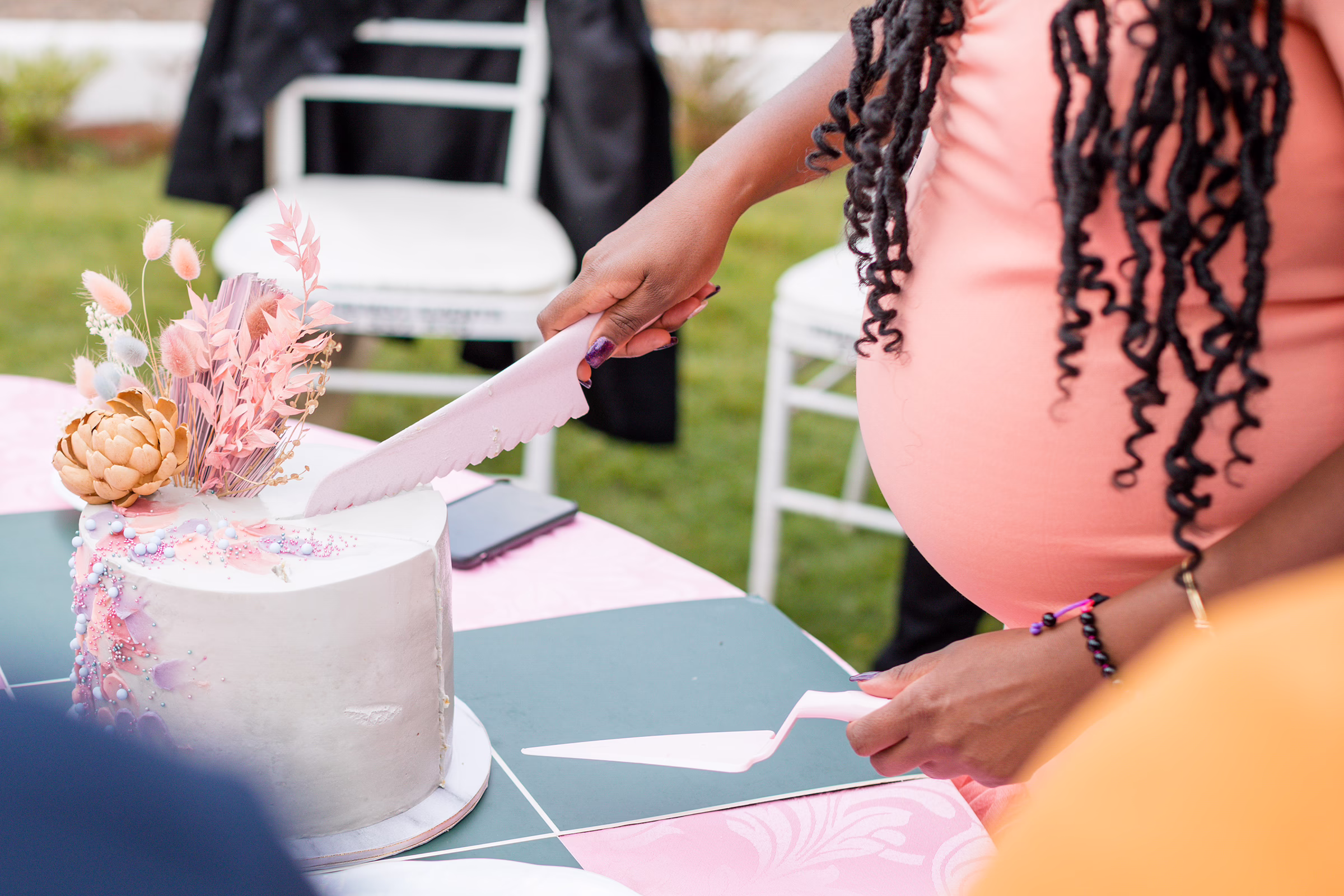 baby shower cake cutting celebration gardens winter park - Orlando Celebration Gardens Pregnant woman in coral dress cutting decorated baby shower cake with dried flowers and pampas grass at outdoor celebration Celebration Gardens in Winter Park Florida