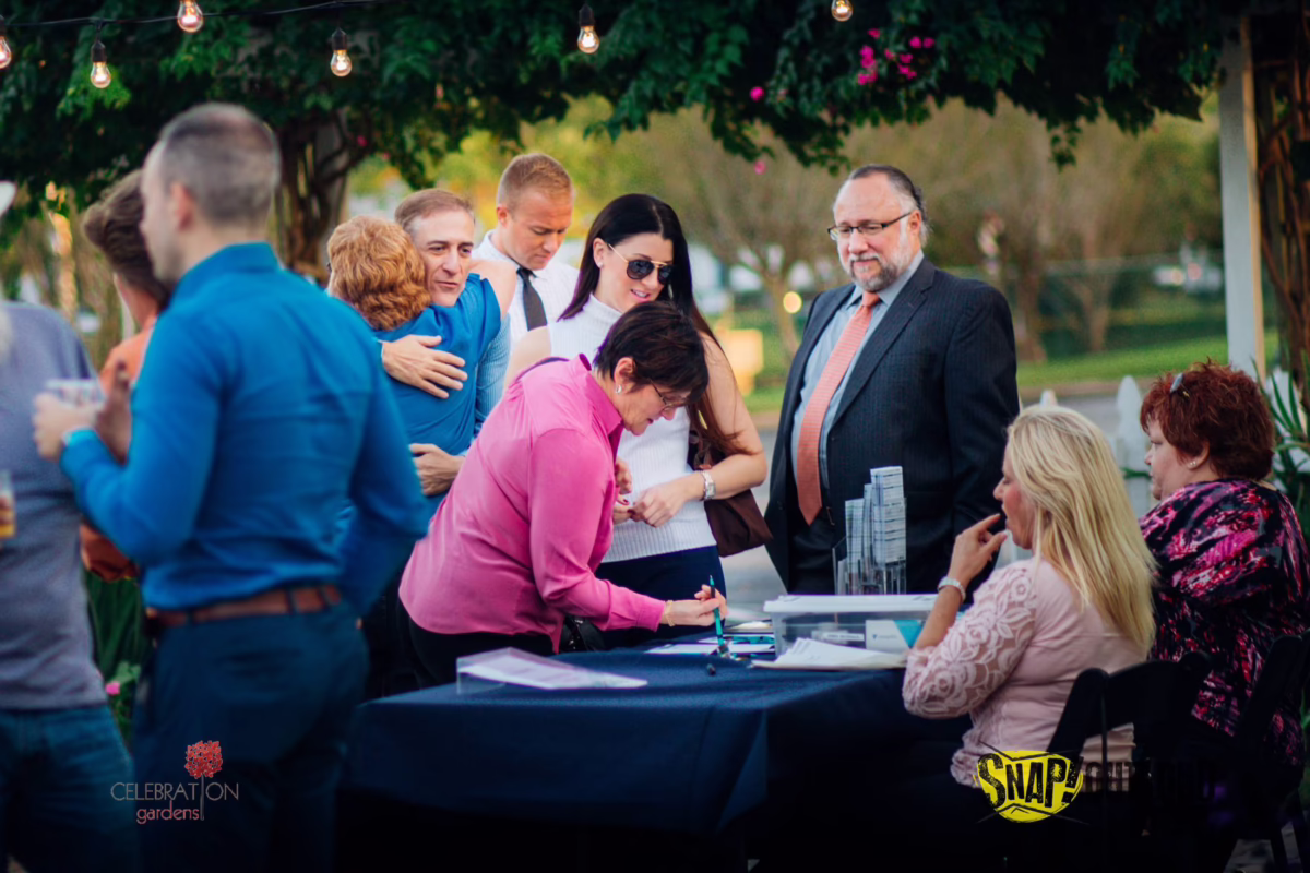 corporate event celebration gardens winter park orlando venue - Pricing Corporate event gathering at Celebration Gardens in Winter Park Orlando with guests signing documents at outdoor table under string lights and greenery