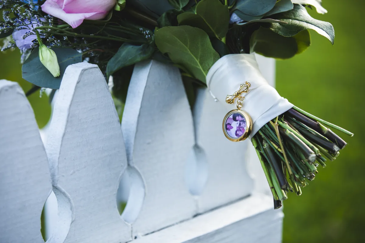 A bridal bouquet with white ribbon and a gold locket charm featuring a photo of a loved one, a meaningful way to honor family members who have passed at an Orlando wedding