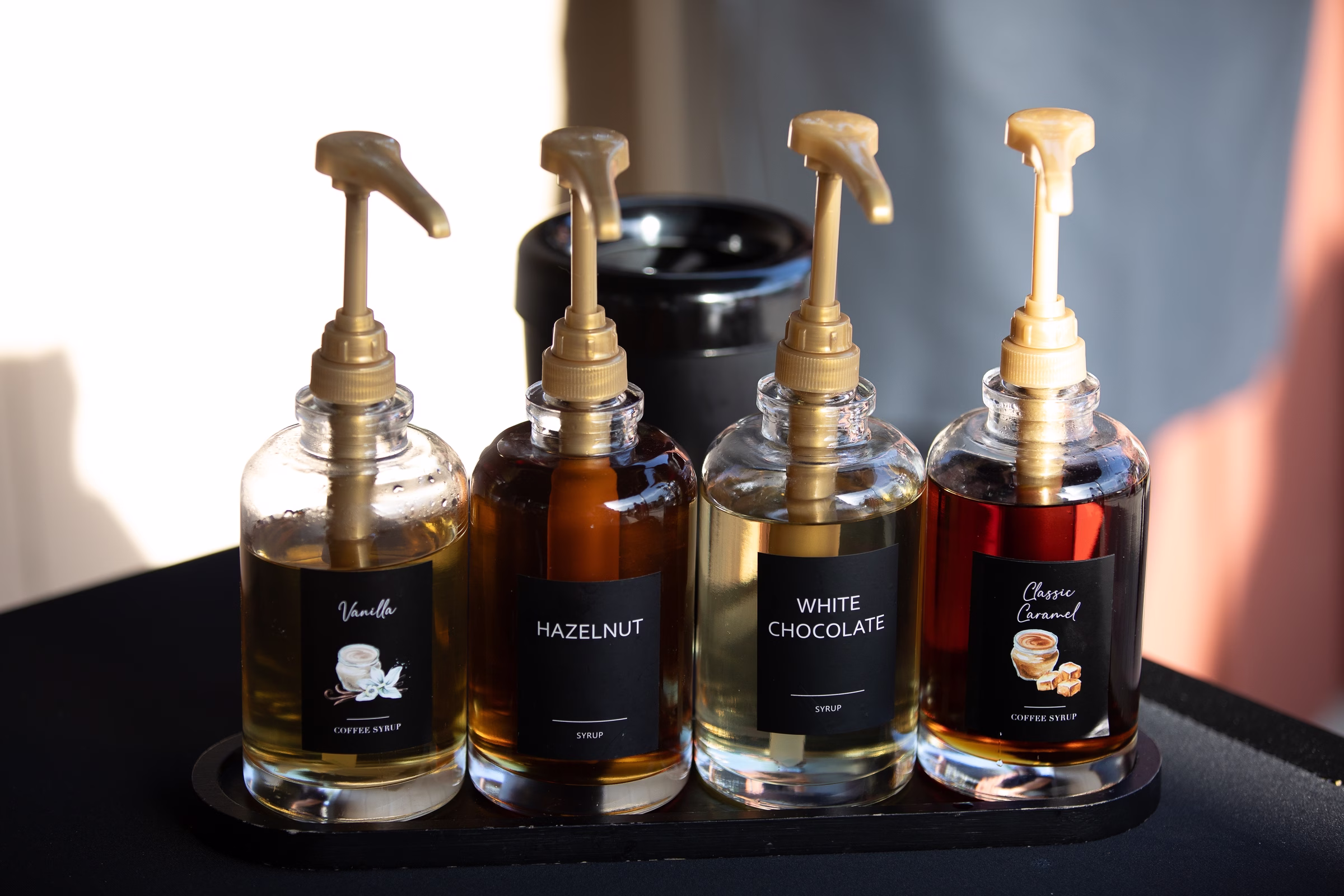 Four glass pump bottles of vanilla, hazelnut, white chocolate, and classic caramel coffee syrups displayed on a tray at a wedding reception at Orlando Celebration Gardens in Orlando Florida