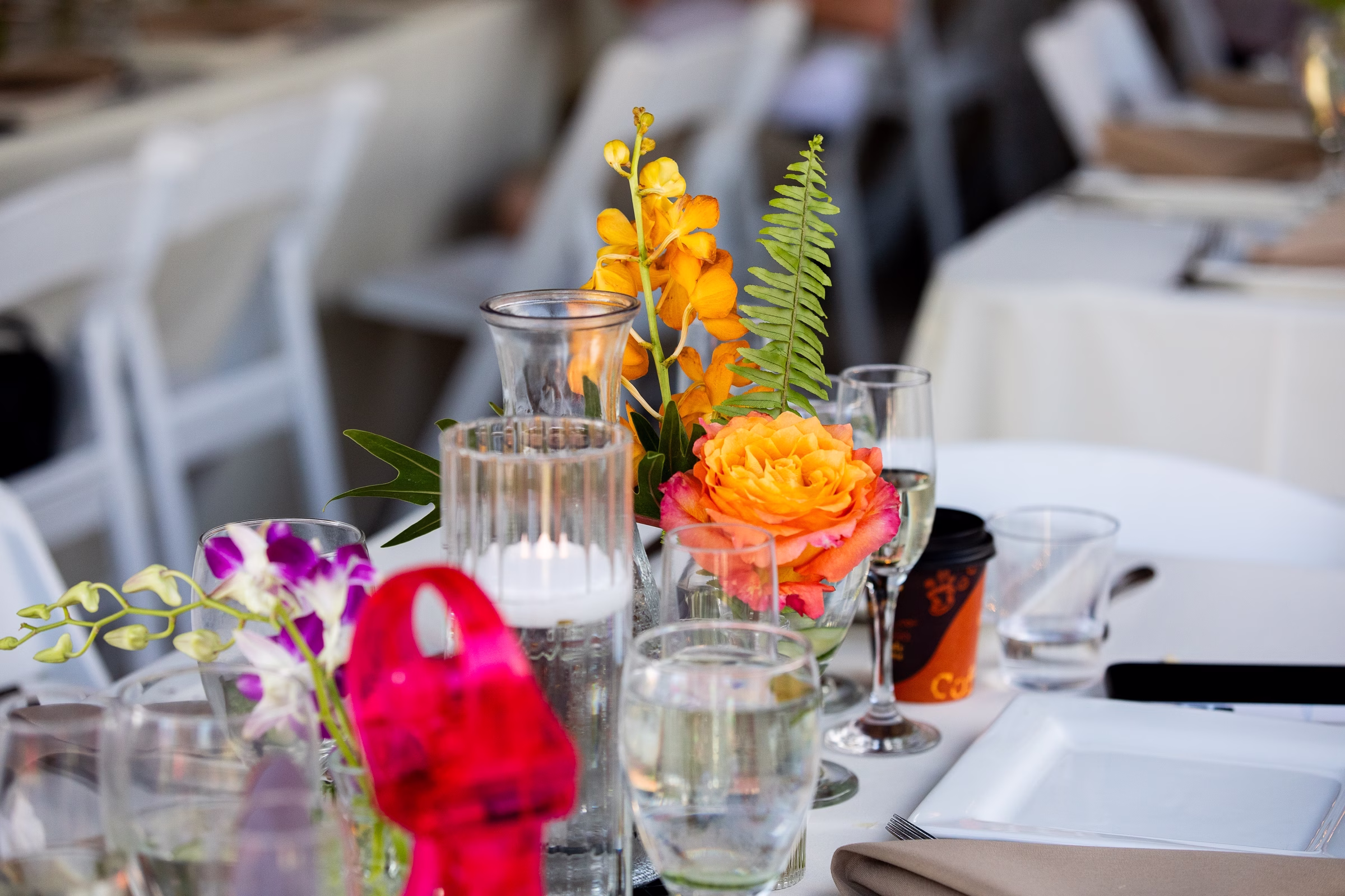 Vibrant tropical wedding centerpiece featuring orange roses, yellow orchids, and fern fronds in glass vases at Orlando Celebration Gardens wedding venue in Orlando Florida