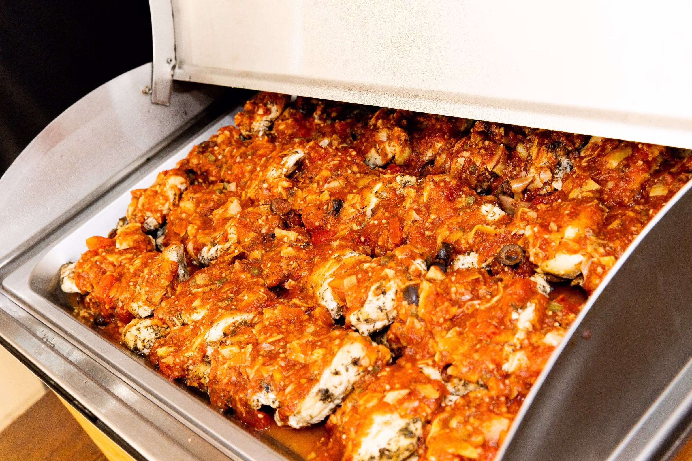 Buffet chafing dish filled with chicken in rich tomato sauce with olives and herbs served at a wedding reception at Orlando Celebration Gardens in Orlando Florida