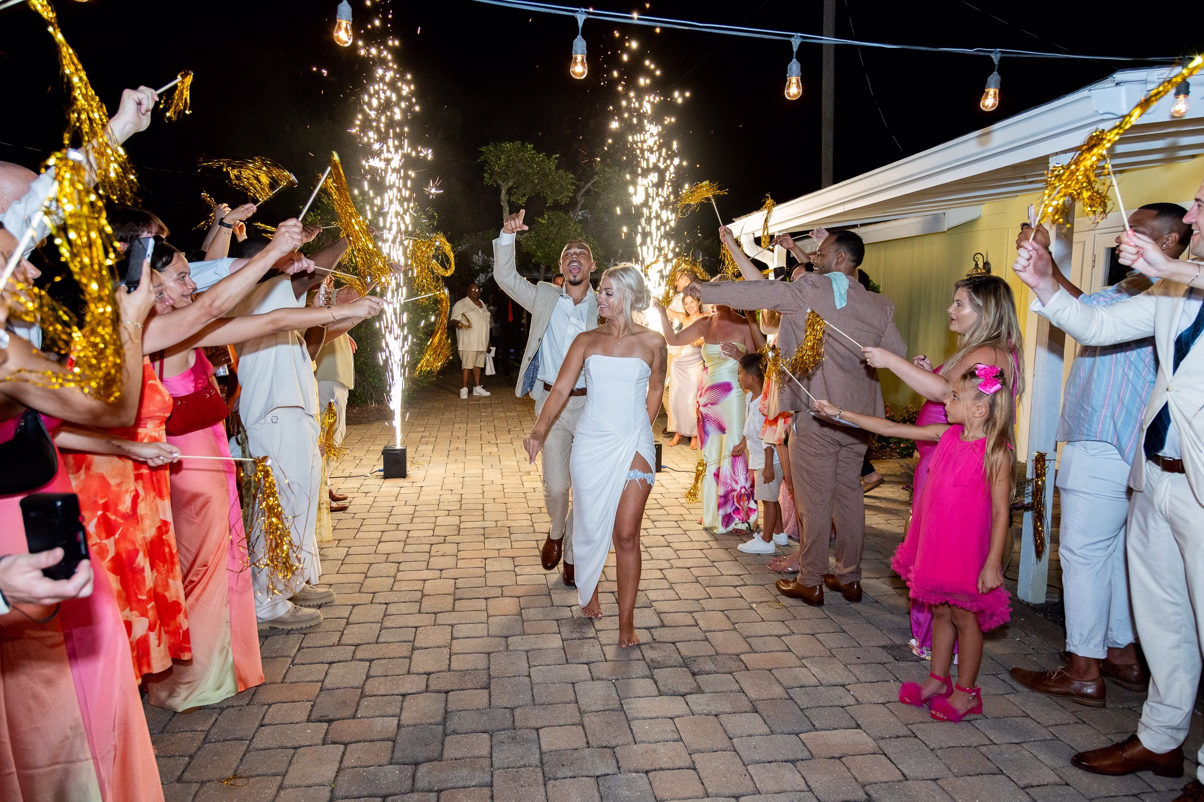 Bride and groom walk through a festive sparkler and gold tinsel wand exit tunnel surrounded by cheering wedding guests at Orlando Celebration Gardens in Orlando Florida